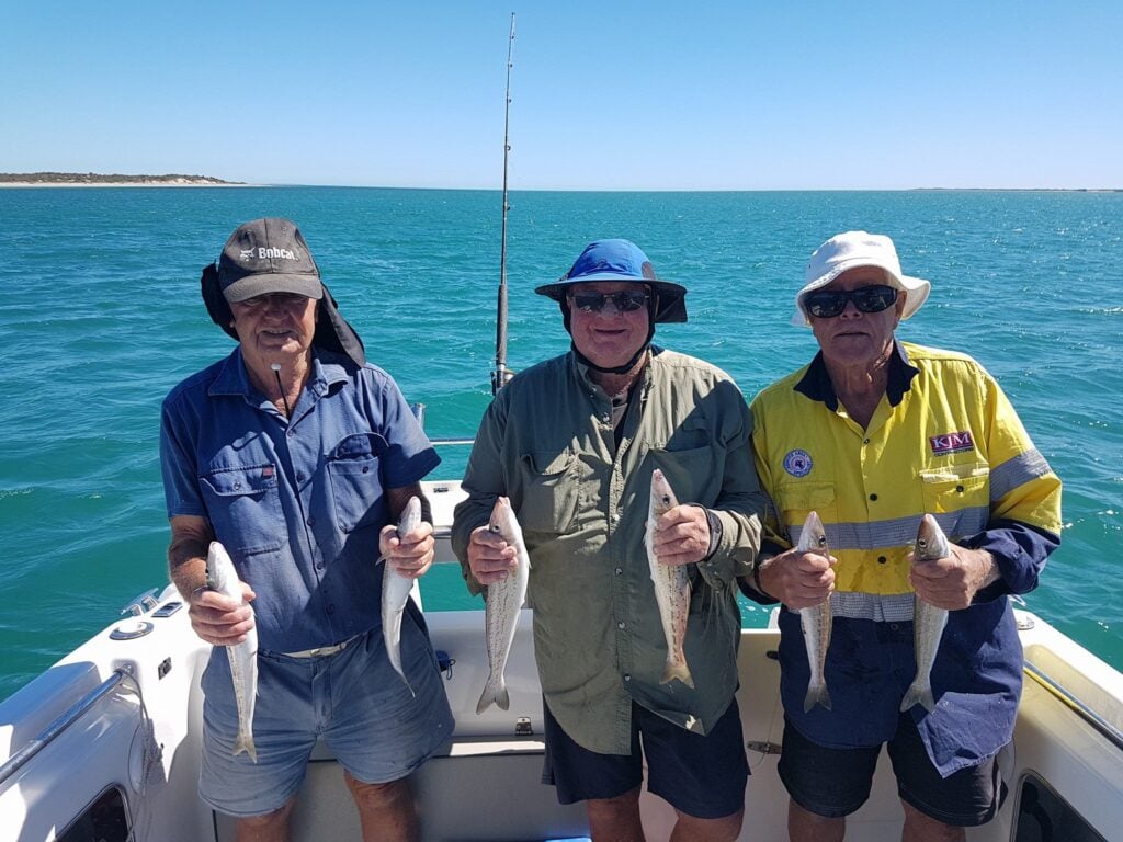 Three men proudly holding their catch while fishing.