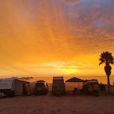Sunset over campsite with palm trees and ocean.