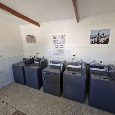 Interior of caravan park laundry with washing machines, laundry sink, bench space, and tiled walls